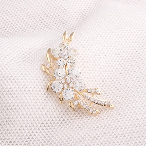Gros plan d'une broche bouquet de fleurs dorée avec cristaux sur un tissu blanc