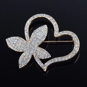 Detailed close-up of a golden heart brooch with crystals on a dark reflective surface