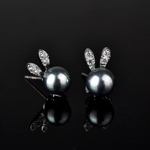 Detail of bunny stud earrings with dark grey pearls and silver crystal ears on black surface