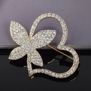 Detail shot of golden crystal heart brooch with rhinestone butterfly design on black surface