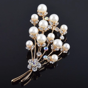 Gros plan sur la broche bouquet avec perles blanches et strass brillants sur métal doré