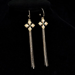 Detail of long gold tassel earrings featuring opal-like stones and emerald green gems