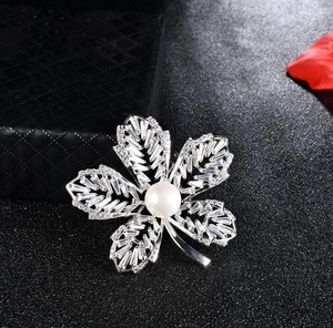 Vue macro d'une broche fleur argentée avec zircons et une perle blanche centrale