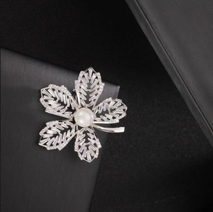 Vue macro d'une broche feuille argentée ornée de zircons et d'une perle centrale blanche