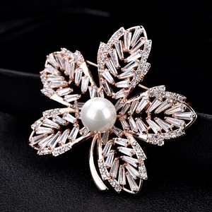 Gros plan sur une broche feuille en or rose avec cristaux de zircone et perle blanche