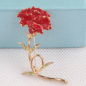Detail shot of a carnation brooch with red petals and green rhinestone leaves on a box