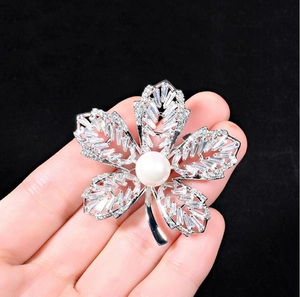 Gros plan d'une broche feuille en zircon avec perle blanche tenue devant un fond sombre