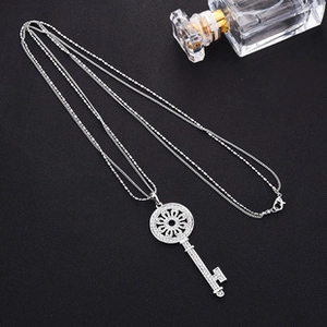 Macro detail of a silver key pendant with sparkling pavé crystals on black fabric