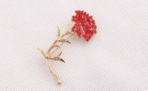 Detail of red carnation brooch with rhinestones and gold alloy stem on white surface