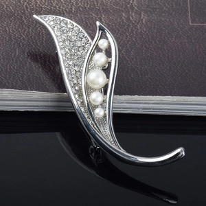 Détail d'une broche argentée courbée ornée de strass et de cinq perles élégantes