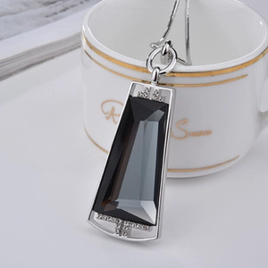 Macro detail of trapezoid gray gemstone pendant with crystal accents on a silver chain