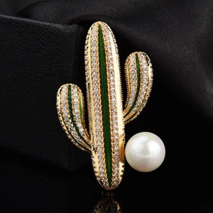 Detailed close-up of a cactus brooch with gold plating, sparkling crystals, and a pearl