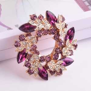 Détail d'une broche florale en cristal violet et or posée sur un coffret cadeau blanc