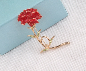 Detail of red carnation brooch with gold stems and green crystal leaves on fabric