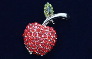 Détail de la broche pomme sertie de strass rouges et verts sur velours bleu