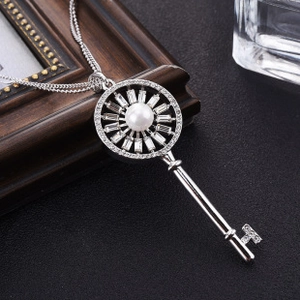 Macro shot of silver key pendant necklace with pearl center and zircon stones on a dark base