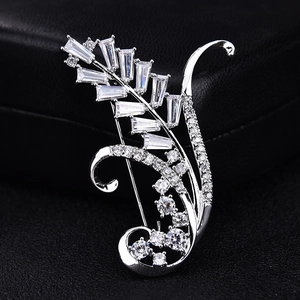 Detailed close-up of a silver wheat-shaped brooch with cubic zirconia on black leather background