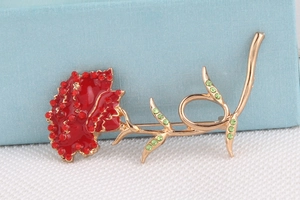 Close-up of carnation brooch with red enamel petals and green crystals on a display box