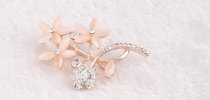 Detail einer roségoldenen Blumenbrosche mit opalen Blütenblättern und weißen Strasssteinen