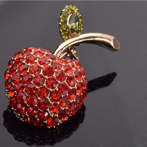 Broche pomme rouge de luxe avec strass et base dorée, montrée avec reflet élégant