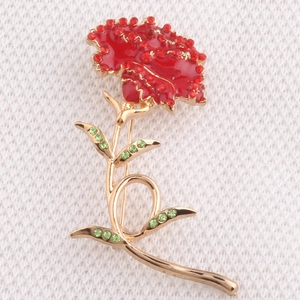 Macro detail of carnation brooch with red enamel petals and green rhinestone leaves