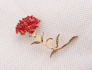 Close-up of carnation flower brooch with red rhinestones and gold-plated green leaf details