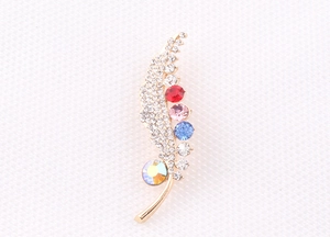 Detailed close-up of a golden feather brooch featuring colorful crystals and micro-pavé rhinestones
