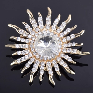 Détail d'une broche soleil dorée ornée de strass en cristal sur une surface noire réfléchissante