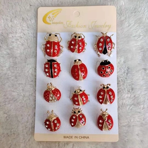 Détail de 12 broches coccinelles en émail rouge et cristaux sur fond en peluche blanche