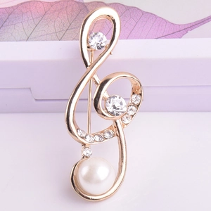 Détail d'une broche note de musique dorée avec cristaux brillants et perle blanche
