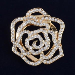 Exquise broche rose dorée avec cristaux scintillants et pétales sur un fond noir texturé