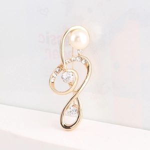 Broche élégante noeud musical doré avec perle et cristaux scintillants sur marbre