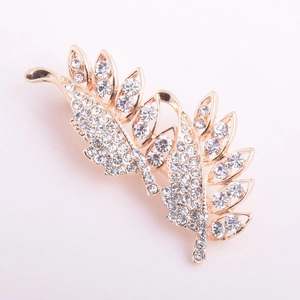 Vue détaillée d'une broche feuille dorée avec incrustation de strass blancs sur fond rose