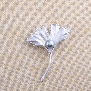 Silver ginkgo leaf brooch with grey pearl and rhinestones on beige fabric background