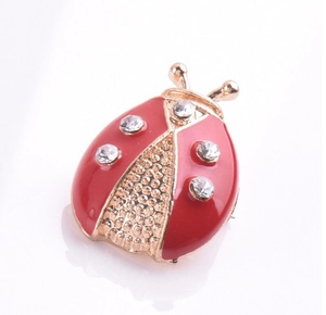 Détail macro d'une broche coccinelle en émail rouge avec strass et cadre en alliage doré