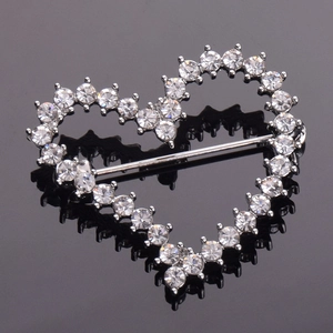Close-up of heart-shaped brooch with white rhinestones and silver metal on black background