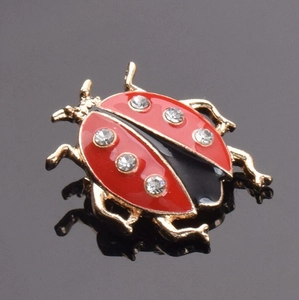 Détails d'une broche coccinelle en émail rouge ornée de cristaux brillants et dorés