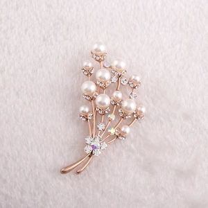 Vue macro d'une broche fleurie or rose avec des perles blanches et des strass