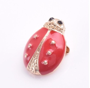 Vue détaillée d'une broche coccinelle en émail rouge avec bords dorés et yeux en gemmes noires