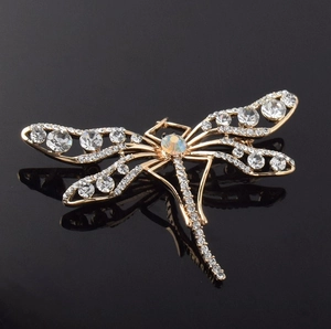 Vue détaillée d'une broche libellule dorée ornée de cristaux sur une surface noire réfléchie