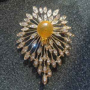 Detailed close-up of golden sunflower brooch with yellow amber stone and zircon crystals
