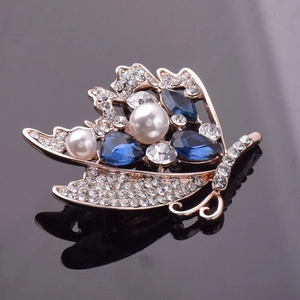 Gros plan d'une broche papillon dorée avec des gemmes bleues et des perles blanches