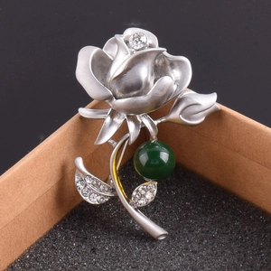 Détail d'une broche rose argentée avec cristaux et perle verte sur boîte cadeau