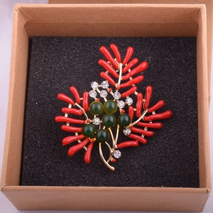 Détail d'une broche corail rouge avec des perles vert foncé et des cristaux étincelants