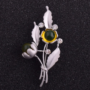 Detail einer floralen Brosche mit matten Silberblättern, grünen Harzsteinen und Kristallen