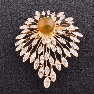 Detailed close-up of a golden radial brooch featuring a green gemstone and white rhinestones