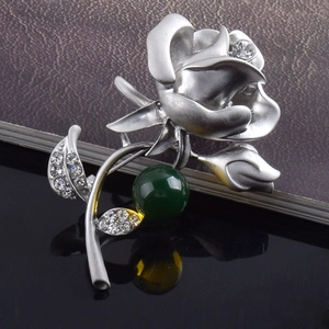Détail d'une broche fleur en argent mat sertie de strass avec une perle verte élégante