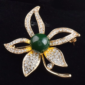 Eleganter goldener Blumenanstecker mit weißen Kristallen und grünem Edelstein auf Samt