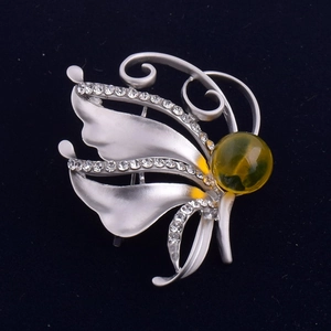 Détail d'une broche papillon argentée avec strass et perle d'ambre sur support bleu foncé
