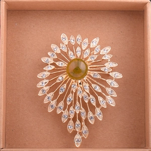 Macro shot of gold floral brooch featuring green resin gemstone and white crystal petals